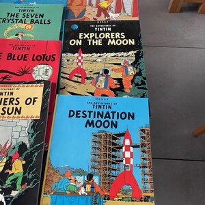 Peut inclure: Plusieurs bandes dessin&eacute;es Tintin, avec des titres comme "L'&Icirc;le Noire", "Les Cigares du Pharaon", "Les Sept Boules de Cristal", "On a march&eacute; sur la Lune", et "Objectif Lune". Les couvertures sont illustr&eacute;es.