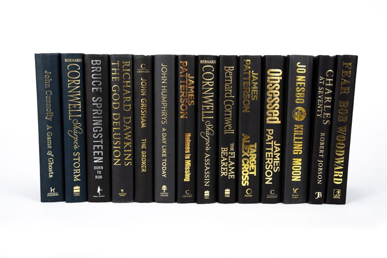 May include: A collection of hardcover books with black covers and gold lettering. Titles include "Sharpe's Storm," "The God Delusion," and "Killing Moon." The books are arranged in a row against a white background.
