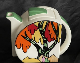 May include: White ceramic teapot with a stylized tree design in shades of orange, yellow, green, and black. The teapot has a green lid and a handle.
