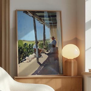 Op de afbeelding: Een ingelijst aquarel schilderij van twee mensen die op een veranda zitten met een houten leuning. Het schilderij is geplaatst tegen een blauwe lucht met witte wolken. Het schilderij hangt aan een muur met een houten lamp op een tafel eronder.