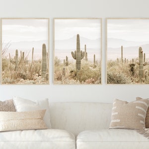 May include: A set of three framed prints featuring a desert landscape with tall cacti and a hazy mountain range in the background. The prints are in a minimalist style with a muted color palette.