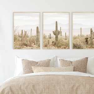 May include: Three framed prints of a desert landscape with tall cacti in the foreground and mountains in the background. The prints are in a muted color palette of beige, brown, and green.