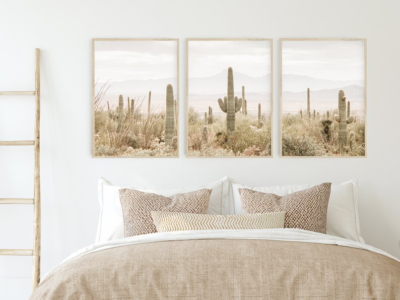 May include: Three framed prints of a desert landscape with tall cacti in the foreground and mountains in the background. The prints are in a muted color palette of beige, brown, and green.