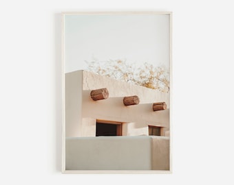 May include: A framed print featuring a southwestern architectural detail. The image showcases a white stucco building with three wooden beams protruding from the wall. The sky is a pale blue, and the overall aesthetic is minimalist and serene.