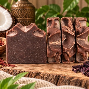 May include: Four rectangular bars of dark brown soap with a smooth front face and textured, swirled tops. The soap bars are arranged in a row, displaying a deep cocoa-colored hue with subtle variations in tone across the sculpted surfaces.