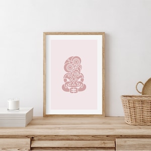 Könnte beinhalten: Ein gerahmter Druck mit rosa Hintergrund und einer weißen Umrandung eines traditionellen Maori-Tiki-Designs.