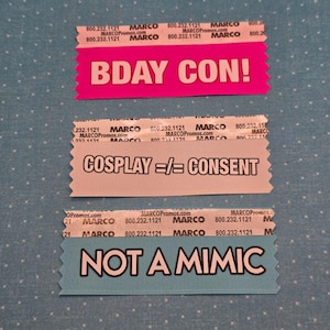 Puede incluir: Tres entradas de evento coloridas con texto. La entrada superior es rosa con "BDAY CON!". La entrada del medio es gris claro con "COSPLAY =/= CONSENT". La entrada inferior es azul claro con "NOT A MIMIC".