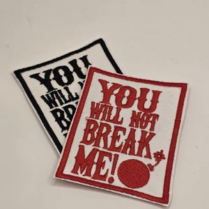 May include: Two rectangular patches with embroidered text. One patch is white with black text that reads "YOU WILL..." The other patch is white with red text that reads "YOU WILL NOT BREAK ME!".
