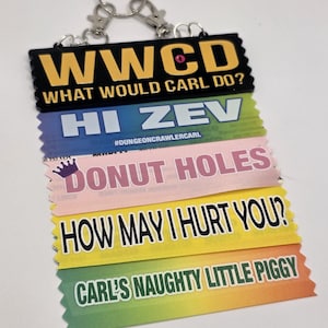 May include: A multi-layered keychain with various phrases. The top layer reads "WWCD WHAT WOULD CARL DO?" in yellow on black. Other layers include "HI ZEV", "DONUT HOLES", "HOW MAY I HURT YOU?", and "CARL'S NAUGHTY LITTLE PIGGY".