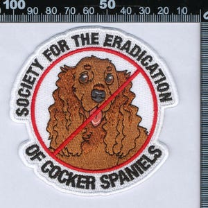 Puede incluir: Un parche bordado circular que presenta un perro Cocker Spaniel marrón en el centro, rodeado por un círculo rojo con una línea diagonal. El texto "SOCIETY FOR THE ERADICATION OF COCKER SPANIELS" está bordado en negro alrededor del borde.