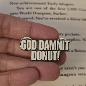 Może przedstawiać: Prostokątna emaliowana przypinka z napisem "GOD DAMNIT DONUT!" pogrubionymi, białymi literami na czarnym tle. Przypinka ma srebrną obwódkę.