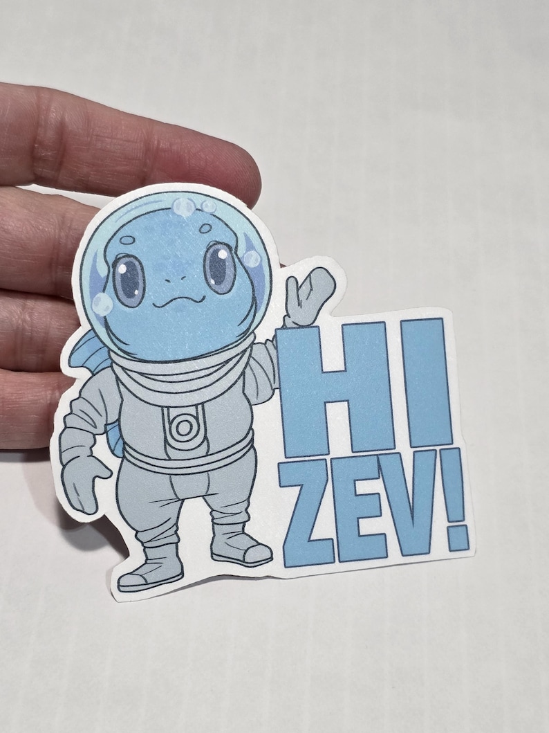 May include: A sticker featuring a cartoon character in a spacesuit with a bubble helmet. The character is light blue with large eyes and a smiling mouth. The text "HI ZEV!" is in blue block letters.