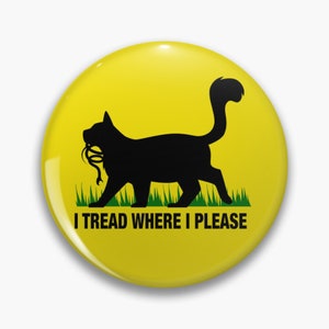 Puede incluir: Un gato negro con una cola amarilla camina sobre hierba verde. El gato lleva una cuerda en la boca. El texto "I tread where I please" está debajo del gato.