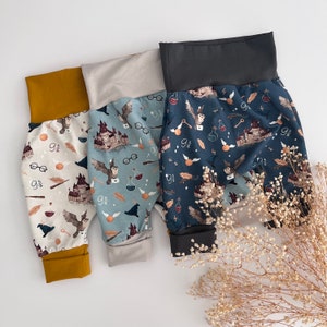 Könnte beinhalten: Drei Paar Kinderhosen mit Harry-Potter-Motiv. Die Hosen sind aus einem weichen, bequemen Stoff gefertigt und zeigen verschiedene magische Designs, darunter Eulen, Zauberstäbe und das Hogwarts-Schloss. Die Hosen sind in Blau, Grau und Senfgelb erhältlich.