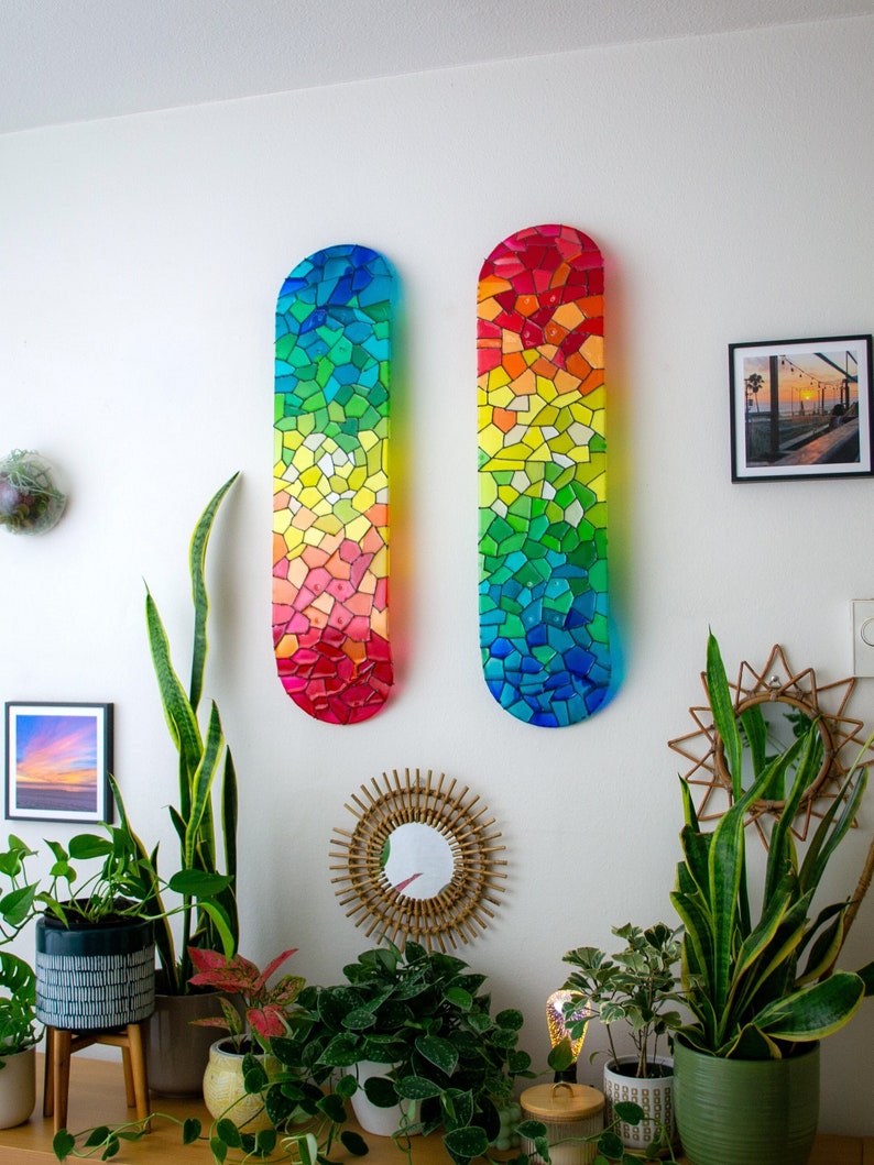 Two rainbow stained glass skateboard decks hanging on wall casting colorful shadows.