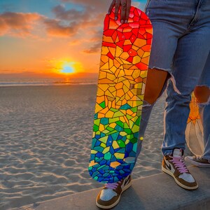 Rainbow stained glass skateboard art at beach during sunset