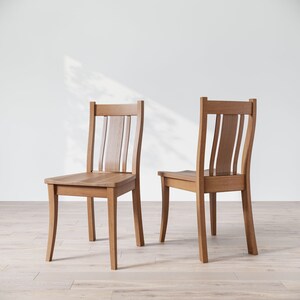 May include: Two wooden chairs with a light brown finish. The chairs have a slatted back and a curved seat.