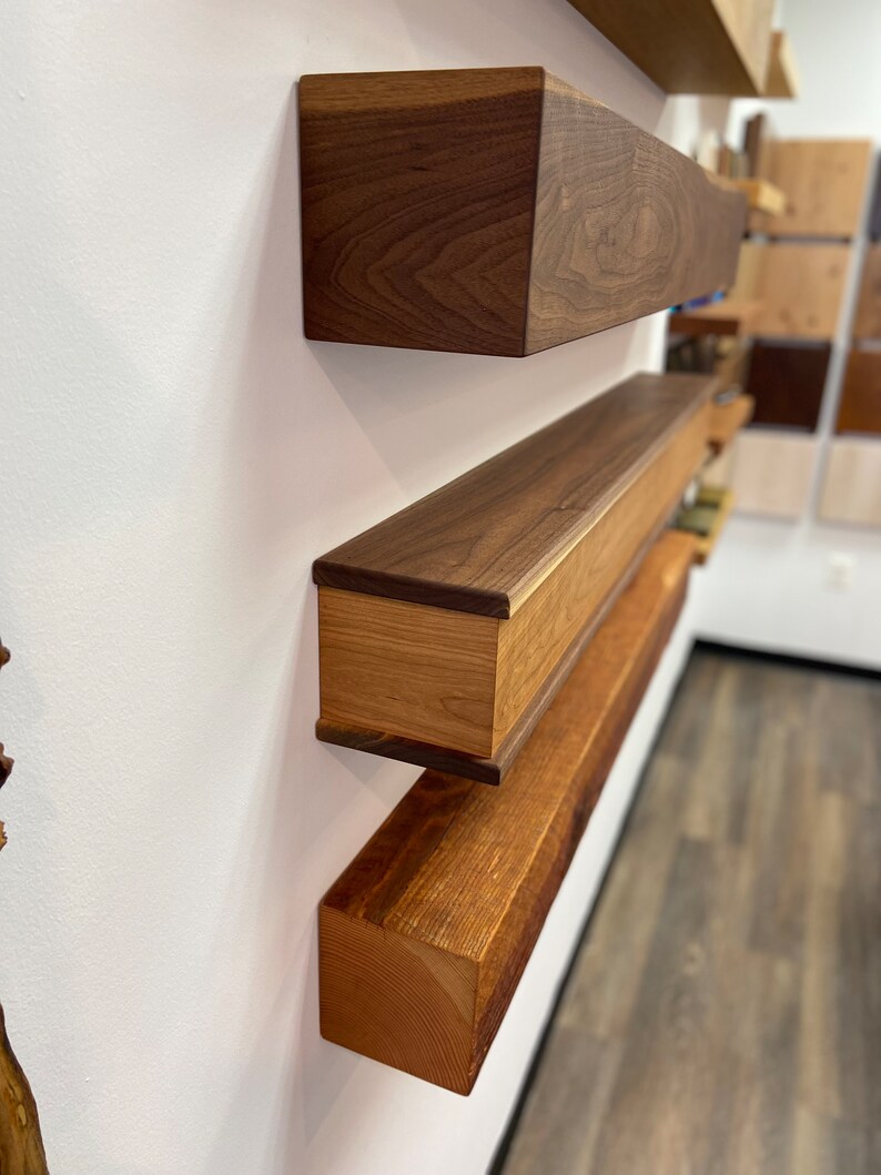 May include: Three wooden shelves mounted on a white wall. The shelves are made of different types of wood, including walnut and pine. The shelves are all different sizes and shapes.