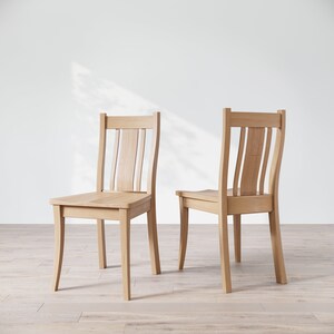 May include: Two wooden chairs with a light brown finish. The chairs have a simple design with vertical slats on the back and curved legs.