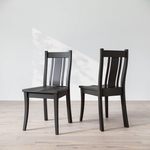 May include: Two black wooden chairs with a simple, classic design. The chairs have a slatted back and a curved seat.