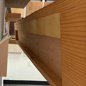 May include: Close-up of the underside of a wooden shelf, showing the construction with multiple layers of wood and a groove for a shelf support.