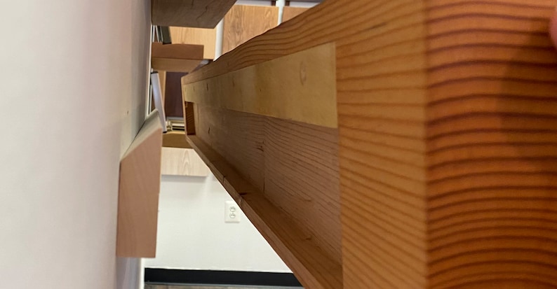 May include: Close-up of the underside of a wooden shelf, showing the construction with multiple layers of wood and a groove for a shelf support.