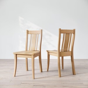 May include: Two wooden chairs with a light brown finish. The chairs have a simple design with a curved back and four legs.