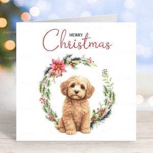 Könnte beinhalten: Weihnachtskarte mit einer Aquarellillustration eines Golden Doodle-Welpen in einem Kranz aus Grün, Beeren und einem Weihnachtsstern. Die Worte "Merry Christmas" sind in roter Schrift über dem Welpen geschrieben.