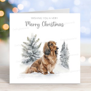 Tarjeta navideña de perro salchicha (de pelo largo y rojo). "Feliz Navidad" con escena invernal, 15 x 15 cm.