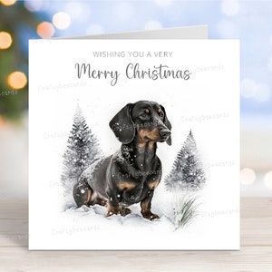 Tarjeta navideña de perro salchicha (pelo liso, negro y fuego). "Feliz Navidad" con escena invernal, 15 x 15 cm.