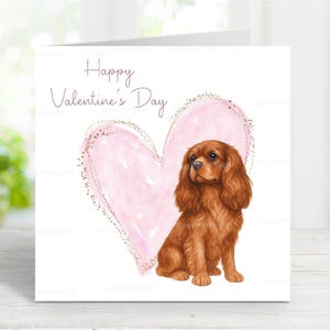 Può includere: Biglietto di San Valentino con un'illustrazione ad acquerello. Mostra un cuore rosa con glitter dorati e un cane Cavalier King Charles Spaniel. Il testo "Happy Valentine's Day" è scritto sopra.