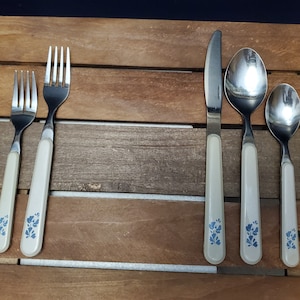 Puede incluir: Conjunto de cinco piezas de cubiertos plateados con diseños florales azules en los mangos. El conjunto incluye un cuchillo, dos tenedores y dos cucharas.