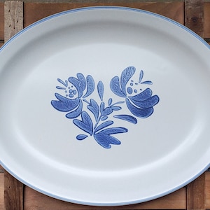 May include: White oval serving platter with a blue floral design. The design features a stylized flower with leaves.