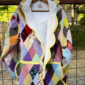 May include: A colorful patchwork jacket with a hood, featuring a variety of diamond-shaped fabric pieces in various colors and patterns. The jacket has a white interior and is trimmed with yellow. It is hanging on a wooden hanger.