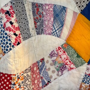 May include: Close-up of a vintage quilt with a white background and colorful, patterned fabric strips. The strips are arranged in a circular pattern, featuring floral, geometric, and abstract designs in red, blue, pink, and yellow.
