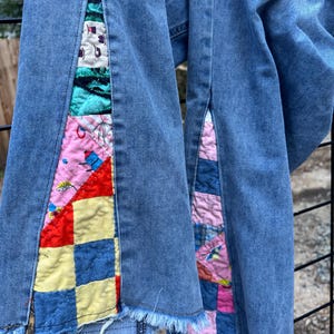 May include: Light blue denim jeans with patchwork fabric inserts. The patchwork features squares of red, yellow, blue, and pink fabric with various patterns. The jeans have a frayed hem.
