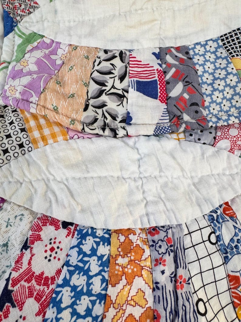 May include: Close-up of a vintage quilt with a variety of patterned fabric strips. The quilt features floral, geometric, and abstract designs in colors like purple, blue, orange, and white. The strips are sewn together with white fabric in between.