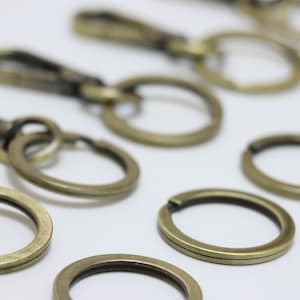 May include: A collection of antique gold key rings and key chain attachments. The key rings are various sizes and shapes, including round, oval, and rectangular.