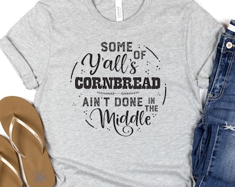 May include: Gray t-shirt with a black graphic that reads "Some of Y'all's Cornbread Ain't Done in the Middle."