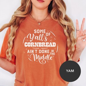 May include: Orange t-shirt with white text that reads "Some of Y'all's Cornbread Ain't Done in the Middle".
