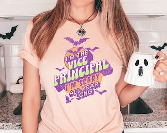 May include: A pink t-shirt with a graphic print of a purple and green text that says "I'm the Vice Principal I'm Scary All Year Long" with a moon and bats in the background.