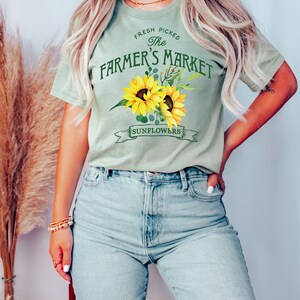 May include: A light green t-shirt with a graphic of sunflowers and the text "Fresh Picked The Farmer's Market Sunflowers".