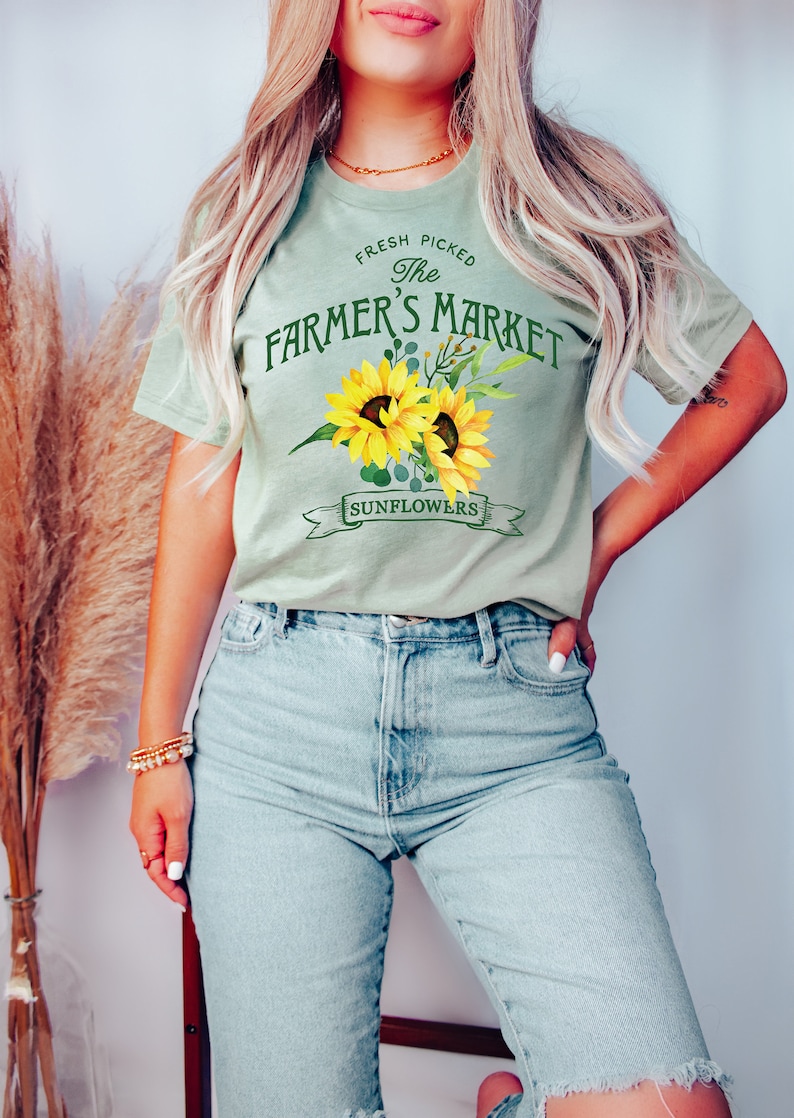 May include: A light green t-shirt with a graphic of sunflowers and the text "Fresh Picked The Farmer's Market Sunflowers".