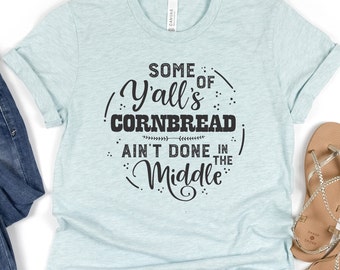 May include: A light blue t-shirt with the text "Some of Y'all's Cornbread Ain't Done in the Middle" printed in black.