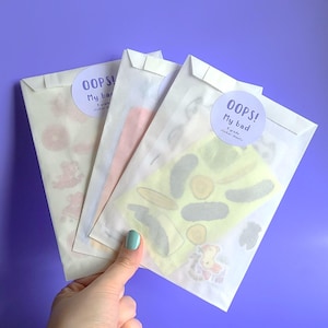 May include: Three white envelopes with sticker sheets inside. The envelopes have a round sticker on the front that says "Oops! My bad" with a small graphic of a sticker sheet. The sticker sheets are visible through the envelopes and feature various colorful designs.