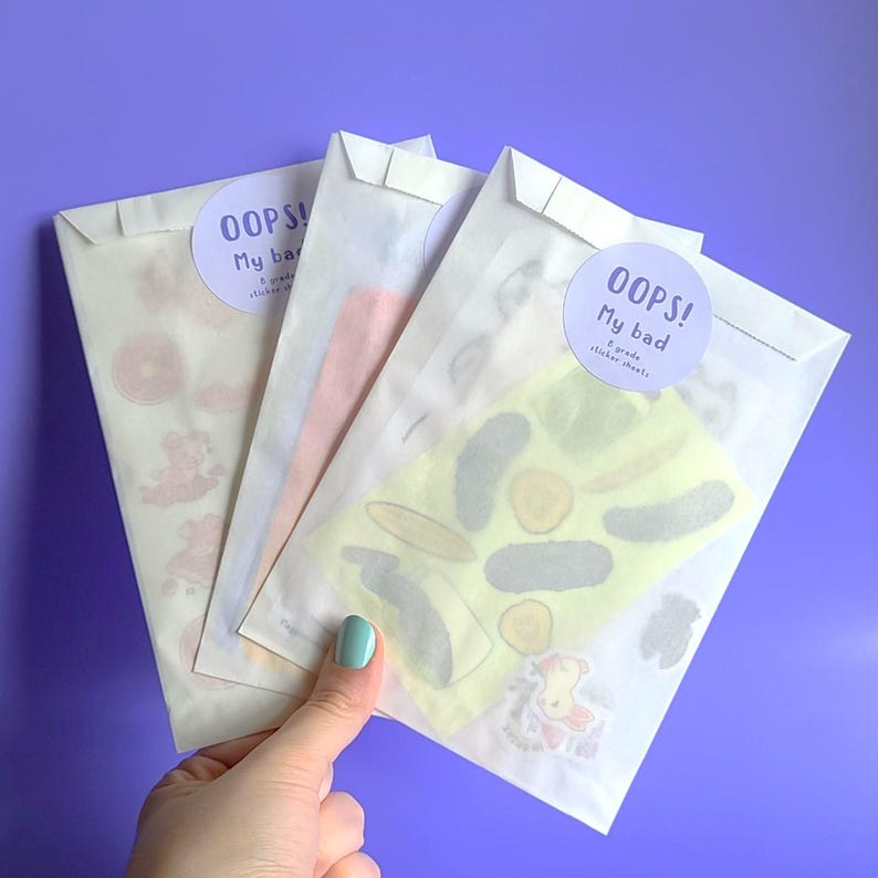 May include: Three white envelopes with sticker sheets inside. The envelopes have a round sticker on the front that says "Oops! My bad" with a small graphic of a sticker sheet. The sticker sheets are visible through the envelopes and feature various colorful designs.