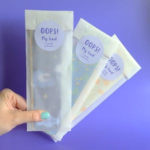 May include: Three white envelopes with a sticker on each. The stickers are round and white with black text that reads "OOPS! My bad 8 grade bookmarks".