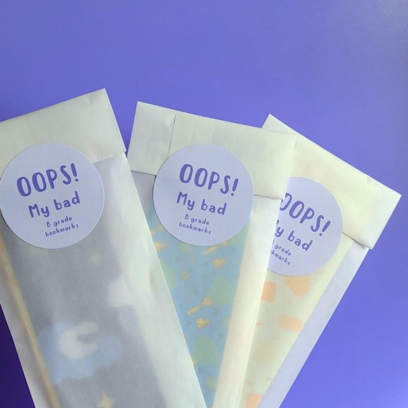 May include: Three white paper envelopes with colorful patterned bookmarks inside. Each envelope has a round sticker with the text "OOPS! My bad B grade bookmarks".