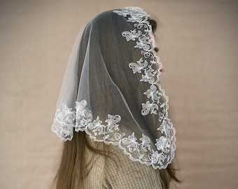 May include: A white chapel veil featuring a delicate floral embroidery pattern along the scalloped edges. The sheer fabric drapes over the head, showcasing intricate white thread work in a botanical design. The word Rutt is printed in the corner.