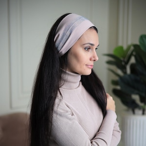 May include: A woman with long dark hair is wearing a light pink headband with a silver sparkly design. She is wearing a light pink ribbed turtleneck sweater.
